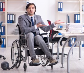 Young handsome employee in wheelchair working in the office