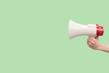 Megaphone in woman hands on a green background.