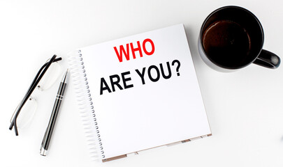 Coffee,glasses,pen and notebook written with WHO ARE YOU , on white background.
