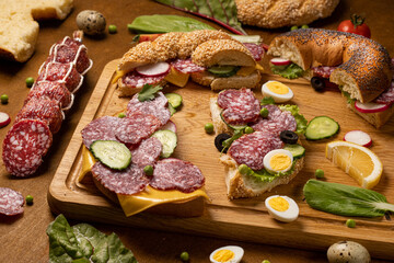 Set of fresh bagels with Salami, radish, cucumber. Top view. Wooden background