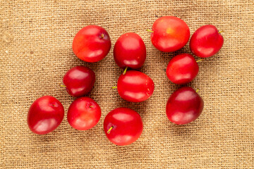 Several organic juicy cherry plums on jute fabric, close-up, top view.