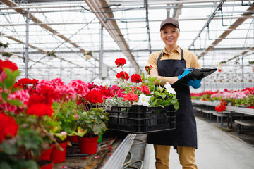 Fototapeta na wymiar Portrait of mature pretty female florist with clipboard in greenhouse