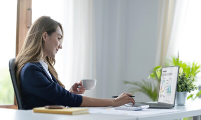 Beautiful young Asian businesswoman smiling holding a coffee mug and laptop working at the office.