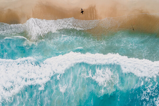 Surfer on tropical sandy beach with blue transparent ocean and waves. Aerial view