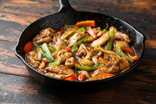 Stir fry pepper chicken with sweet peppers, onion, garlic and ginger in iron cast pan
