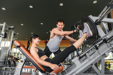 Young Asian male trainer is teaching Asian girls the right exercises in the gym. A young Asian bodybuilder trainer is teaching Asian women the correct use of exercise equipment in the gym.