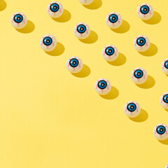Halloween pattern made of plastic eyes on bright yellow background. Happy halloween concept with copy space.