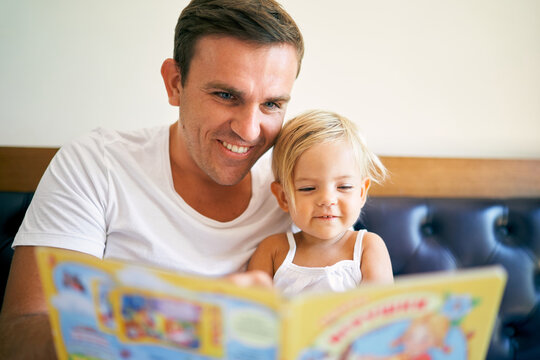 Smiling dad reads a book to a little daughter