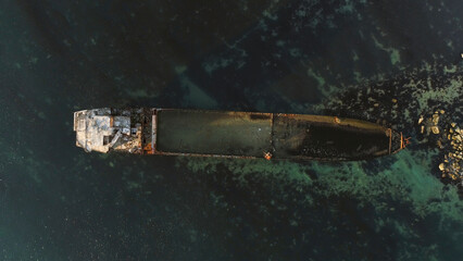 Aerial top view for wrecked ship along the rocky coast in blue water. Shot. Old sunk boat near sea...