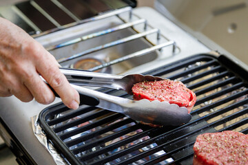 Using tongs to place bacon wrapped filet mignon steak on outdoor camping grill
