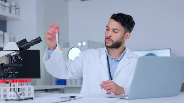 Biologist working with blood collection tubes data and typing information on a laptop. One young male chemist, scientist or healthcare professional doing lab report testing and analyzing samples