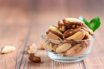 Bowl with tasty Brazil nuts on sack and space for text on  wooden background,