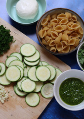 Pasta pesto ingredients on a table. Close up photo of pasta, mozzarella, zucchini, parsley, garlic, onion and pesto sauce. Balanced menu concept. 