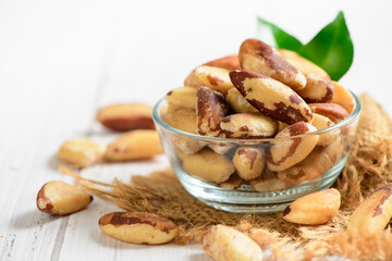 Bowl with tasty Brazil nuts on sack and space for text on white wooden background, Healthy food