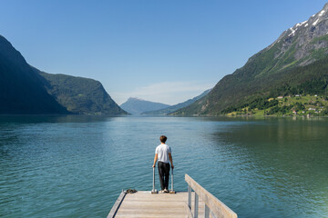 Fototapeta na wymiar person standing at end of pier gazing at blue sky, mountains and water