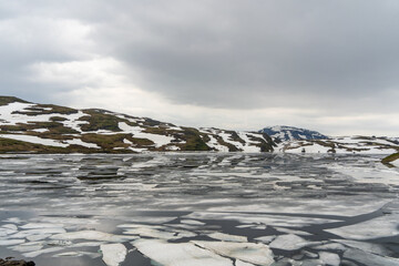 winter landscape with broken ice in lake and rolling hills with snow in background and clouds in sky
