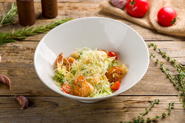 salad caesar with shrimps on white plate on old wooden table
