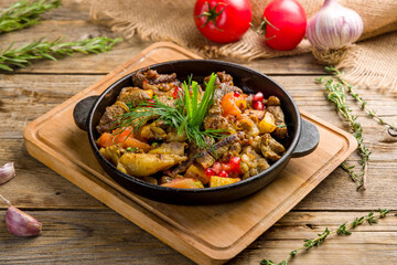 roast lamb with vegetables in Chinese sauce in a hot frying pan on old wooden table