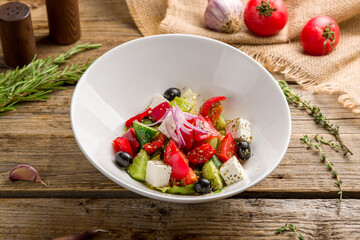 Greek salad with feta on white plate on old wooden table