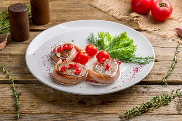 Pork medallions with bacon on white plate on old wooden table