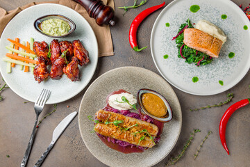 turkey sausages on a plate with cabbage and honey mustard sauce , salmon with spinach and chicken wings on brown table top view