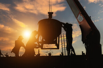 Construction workers pour cement from mortar buckets used by a crane to lift them up against a cold sunset background. - Powered by Adobe