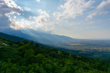 Sun rays going through the clouds over beautiful landscape with mountains and hills in Greece