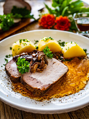Roast pork with mushrooms, sauce and boiled potatoes on wooden table
