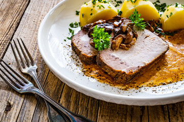 Roast pork with mushrooms, sauce and boiled potatoes on wooden table
 - obrazy, fototapety, plakaty