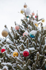 Fir branches covered with snow and bright colorful baubles. Decorated christmas tree outdoors