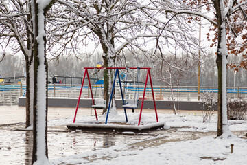 empty playground, bright swing set for children covered with snow on winter background, no people. Cold frosty weather, abandoned city