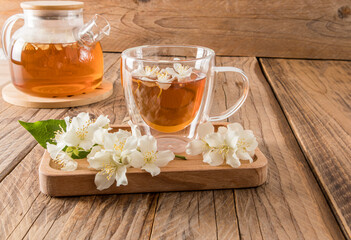 glass transparent cup with fragrant jasmine tea on a wooden tray with the flowers of the plant. wooden rustic table with teapot. tea composition.