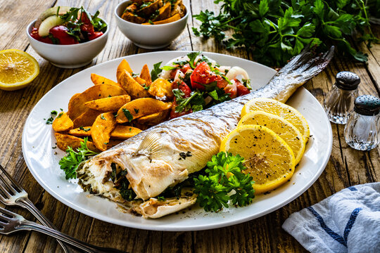 Fried perch with boiled potatoes, lemon and fresh vegetable salad served on wooden table
