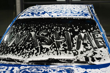 wash me written on the car covered by foam