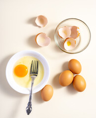 Raw eggs in a glass and white bowl on the table. Flat lay. Broken White Background.