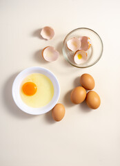 Raw eggs in a glass and white bowl on the table. Flat lay. Broken White Background.