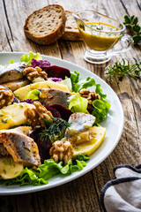 Marinated herrings with roasted beetroots, apple, walnuts  and fresh vegetable leaves on wooden...