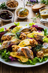Marinated herrings with roasted beetroots, apple, walnuts  and fresh vegetable leaves on wooden table
