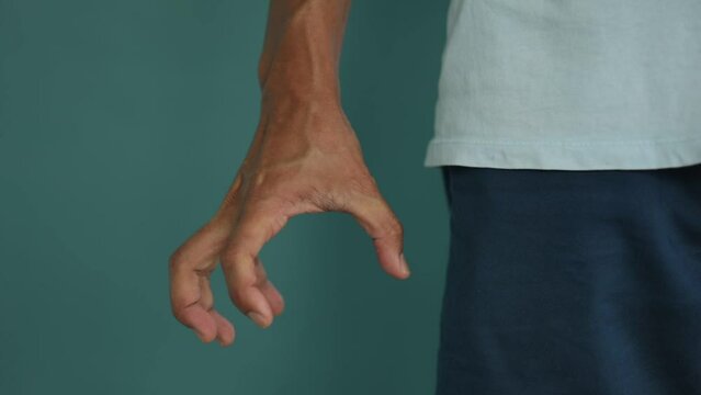 The right hand of an Asian Thai man spread out and tensed his hand until he saw the veins and clenched fist seem angry Or is convulsing, with a dark grip, Isolate green background.