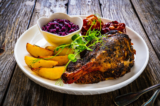 Roast duck thigh with, baked potatoes, fruits and and red cabbage on wooden table
