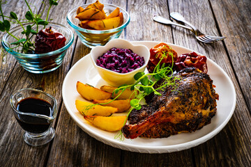 Roast duck thigh with, baked potatoes, fruits and and red cabbage on wooden table
