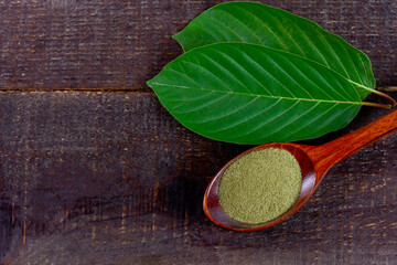Mitragyna Speciosa Korth or kratom powder on wooden spoon with green leaf on rustic wooden table, copy space, top view.