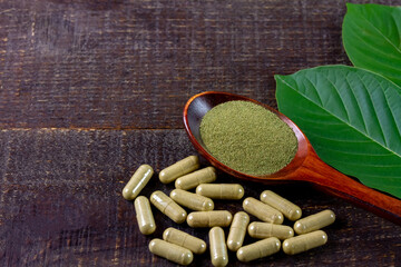 Mitragyna Speciosa Korth or kratom capsules on wooden spoon with green leaf and capsules on rustic wooden table, copy space, top view.
