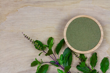 Holy basil powder on wooden bowl with branch on rustic wooden background, top view. Holy basil leaf are useful herbs and food ingredient has a spicy flavor. 