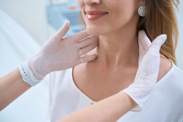 Naklejka premium Dermatologist with hands in gloves touches the patient neck, close-up