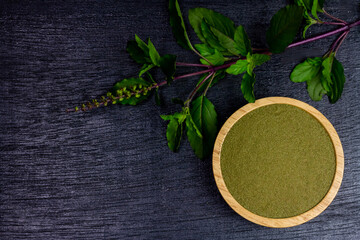 Holy basil powder on wooden bowl with branch on black wooden background, top view. Holy basil leaf...