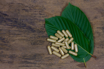 Mitragyna Speciosa Korth or kratom capsules with green leaf on rustic wooden table, top view.
