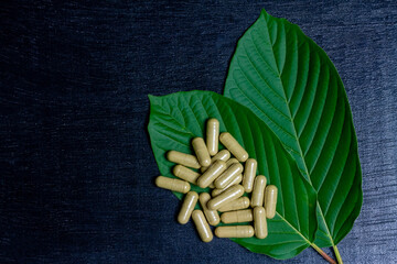 Mitragyna Speciosa Korth or kratom capsules with green leaf on black wooden table, top view, copy...