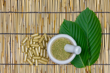Mitragyna Speciosa Korth or kratom capsules with white mortar and pestle and green leaf on wooden...