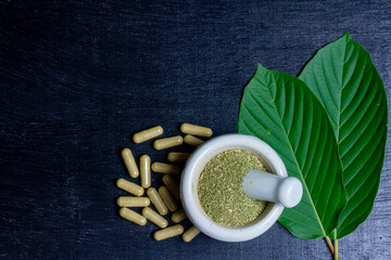Mitragyna Speciosa Korth or kratom capsules with white mortar and pestle and green leaf on black...